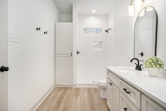 full bathroom with toilet, wood finished floors, vanity, and a tile shower