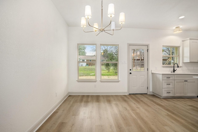 unfurnished dining area featuring a sink, baseboards, plenty of natural light, and light wood finished floors