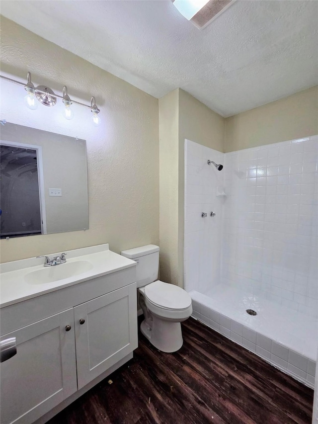 bathroom featuring vanity, wood finished floors, a tile shower, a textured ceiling, and toilet