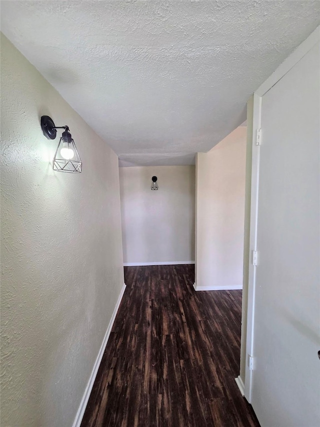 hallway with a textured ceiling, baseboards, and wood finished floors