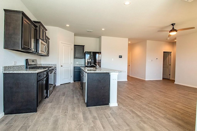 kitchen featuring light wood-type flooring, a center island with sink, stainless steel microwave, recessed lighting, and gas range