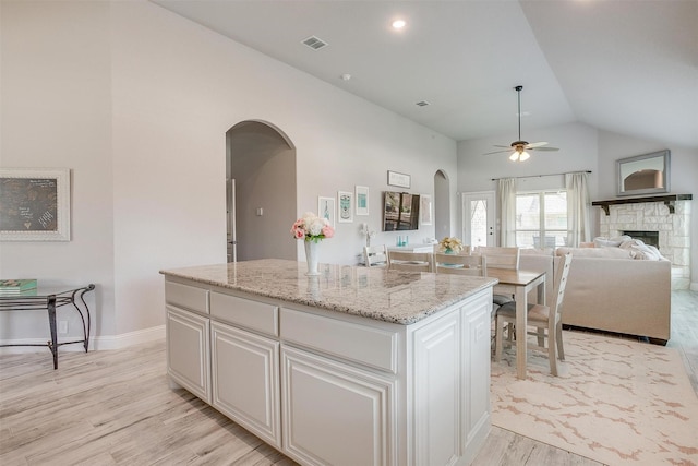 kitchen featuring visible vents, light wood finished floors, a kitchen island, arched walkways, and vaulted ceiling