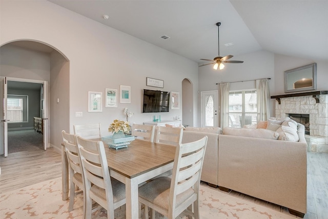 dining area with visible vents, arched walkways, light wood-style floors, a stone fireplace, and lofted ceiling