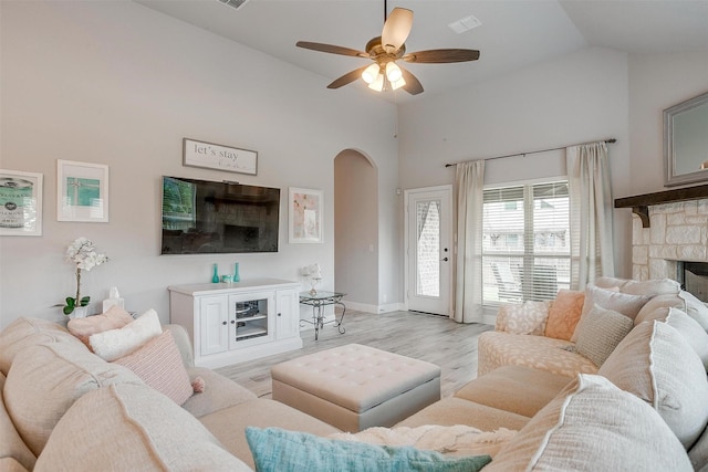 living area featuring light wood finished floors, a fireplace, arched walkways, high vaulted ceiling, and a ceiling fan