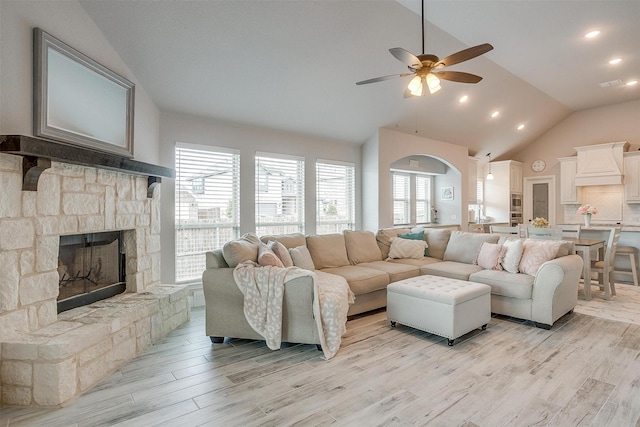 living room with a stone fireplace, recessed lighting, light wood-style floors, high vaulted ceiling, and a ceiling fan