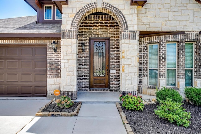 property entrance with an attached garage, brick siding, stone siding, and a shingled roof