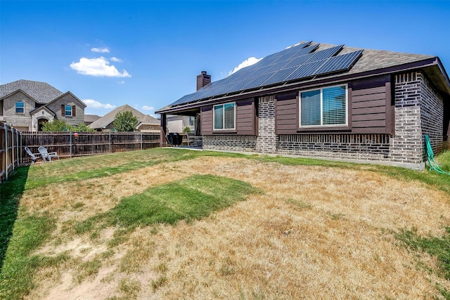 back of property with a lawn, a fenced backyard, brick siding, solar panels, and a chimney