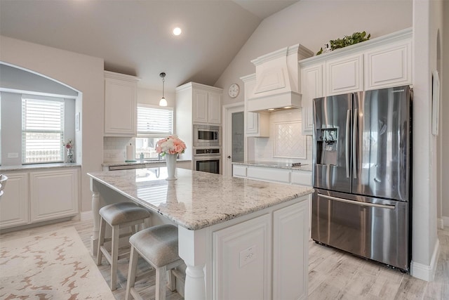 kitchen featuring lofted ceiling, light stone counters, custom exhaust hood, white cabinets, and stainless steel appliances