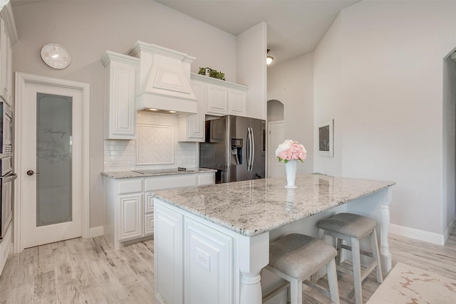 kitchen featuring premium range hood, light stone countertops, appliances with stainless steel finishes, and a breakfast bar area