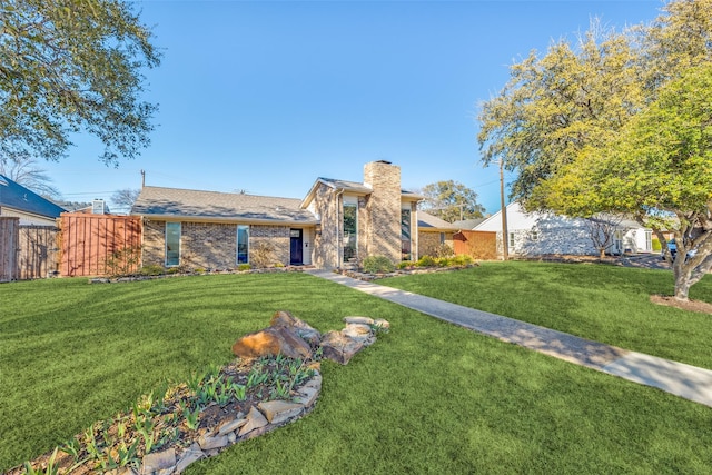 view of front of home featuring a front lawn, brick siding, a chimney, and fence