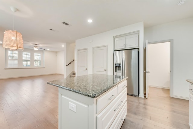 kitchen featuring a center island, ceiling fan, dark stone counters, light wood-style floors, and stainless steel fridge