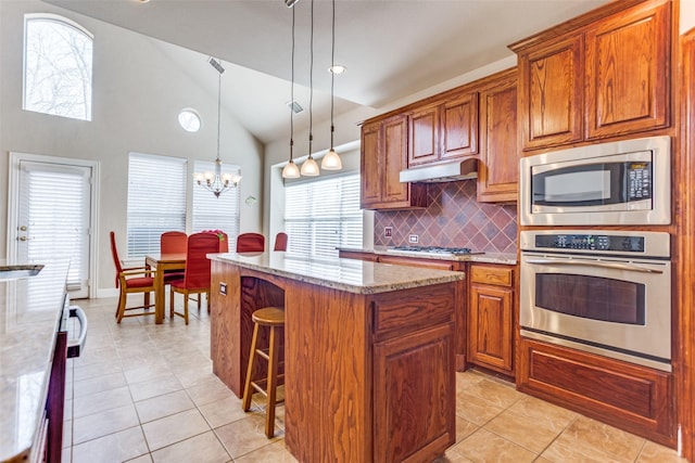 kitchen with a notable chandelier, light stone counters, a kitchen breakfast bar, appliances with stainless steel finishes, and brown cabinetry