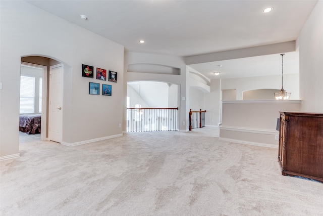 spare room with baseboards, arched walkways, vaulted ceiling, light colored carpet, and a chandelier