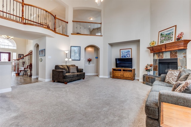 carpeted living room with arched walkways, stairway, a tile fireplace, and baseboards