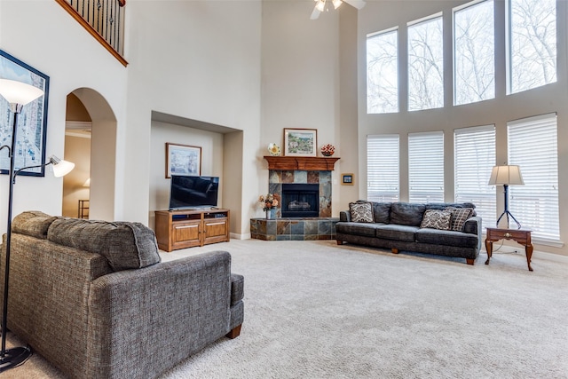 carpeted living room with baseboards, arched walkways, ceiling fan, a towering ceiling, and a tiled fireplace