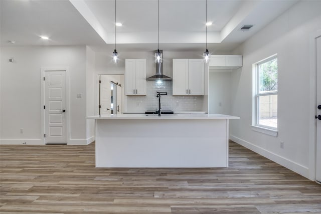 kitchen featuring tasteful backsplash, wall chimney exhaust hood, white cabinetry, and a raised ceiling