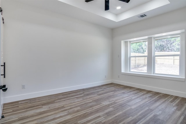 unfurnished room with a tray ceiling, wood finished floors, baseboards, and visible vents