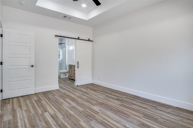 unfurnished bedroom with visible vents, light wood-style flooring, baseboards, and a barn door