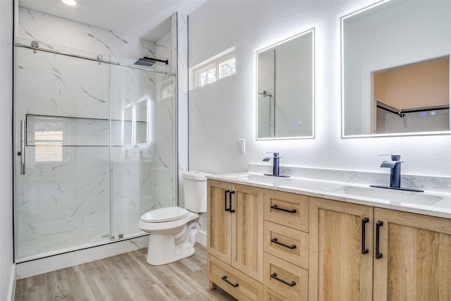 bathroom with wood finished floors, a marble finish shower, double vanity, a sink, and toilet