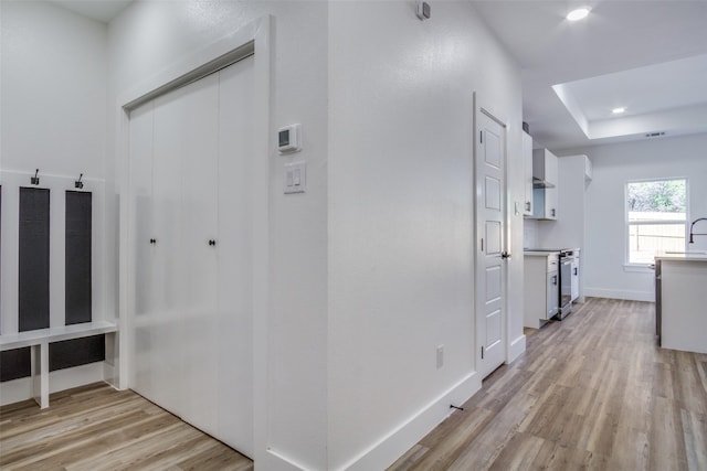 hallway with a tray ceiling, recessed lighting, light wood-style floors, and baseboards