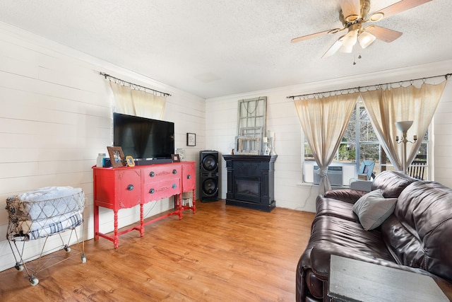 living room with ceiling fan, cooling unit, wood finished floors, a glass covered fireplace, and a textured ceiling