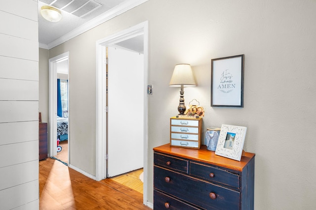 hallway featuring visible vents, wood finished floors, and ornamental molding