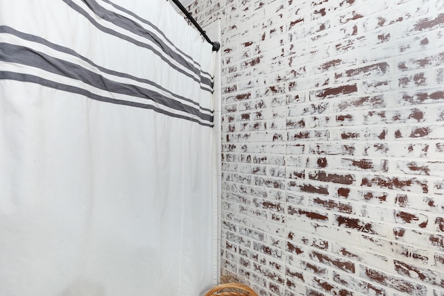 full bath featuring a shower with shower curtain and brick wall