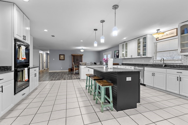 kitchen with light tile patterned floors, a kitchen island, a sink, dobule oven black, and a kitchen bar