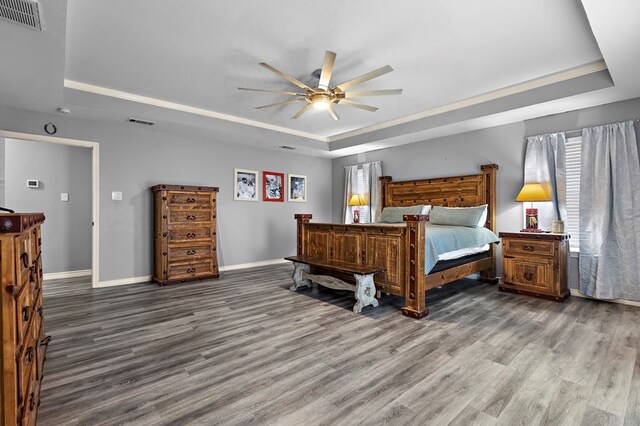 bedroom with a tray ceiling, wood finished floors, visible vents, and baseboards