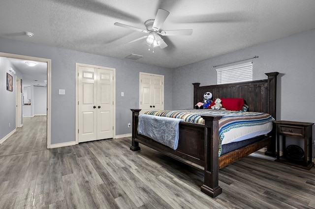 bedroom featuring visible vents, a textured ceiling, wood finished floors, baseboards, and ceiling fan