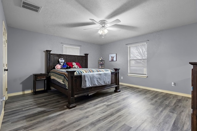 bedroom featuring visible vents, a textured ceiling, baseboards, and wood finished floors