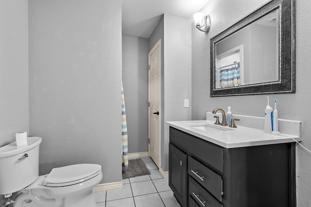 bathroom featuring baseboards, toilet, a textured wall, tile patterned floors, and vanity