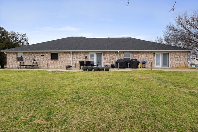 back of property with a lawn, a shingled roof, brick siding, and a patio area