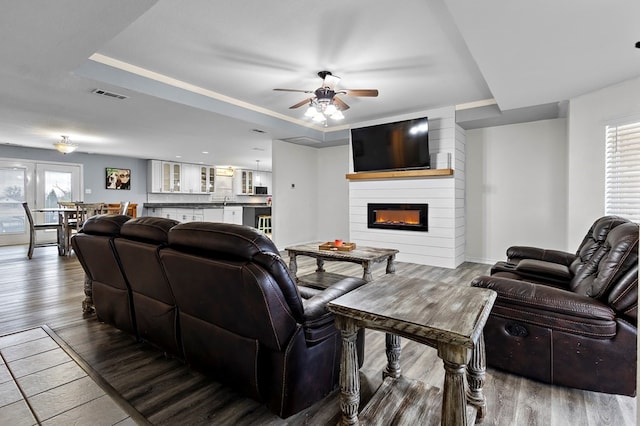 living room featuring visible vents, a large fireplace, a raised ceiling, and wood finished floors