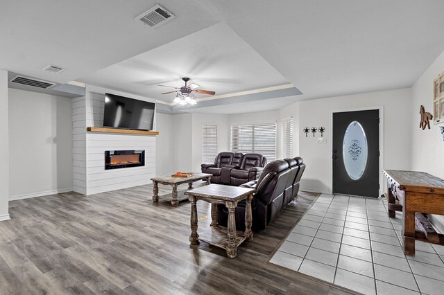 living area featuring a glass covered fireplace, a tray ceiling, and visible vents