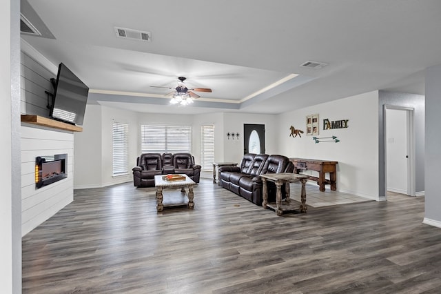 living area with a tray ceiling, visible vents, a large fireplace, and wood finished floors