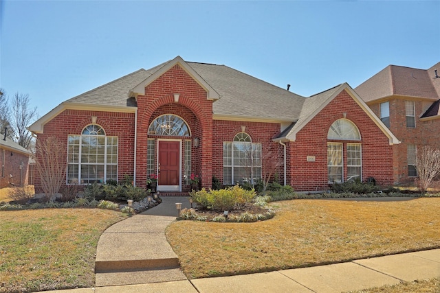 traditional-style home with brick siding, roof with shingles, and a front lawn