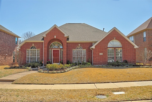 traditional-style home featuring brick siding, roof with shingles, and a front lawn