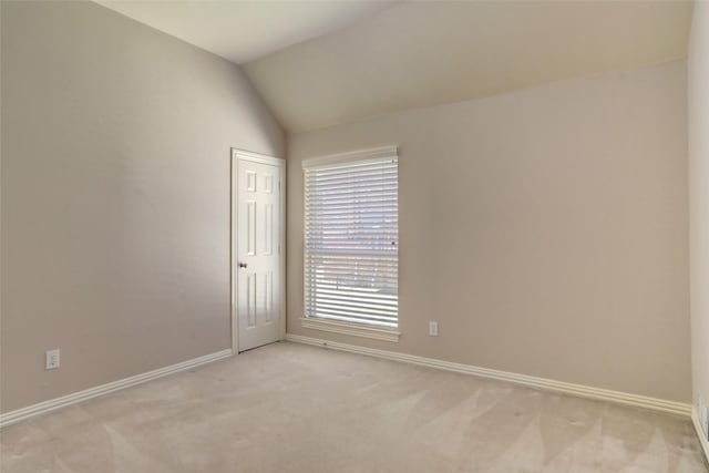 empty room featuring vaulted ceiling, light colored carpet, and baseboards