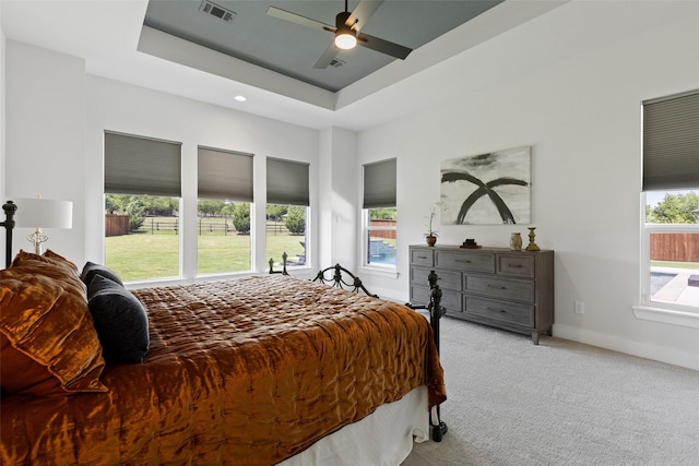 carpeted bedroom featuring visible vents, ceiling fan, a tray ceiling, and baseboards