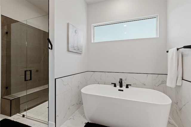 full bath with a stall shower, marble finish floor, tile walls, and a freestanding tub