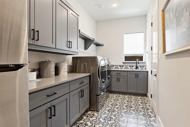 clothes washing area with visible vents, separate washer and dryer, cabinet space, and a sink