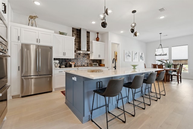 kitchen with a large island, tasteful backsplash, wall chimney exhaust hood, white cabinets, and appliances with stainless steel finishes