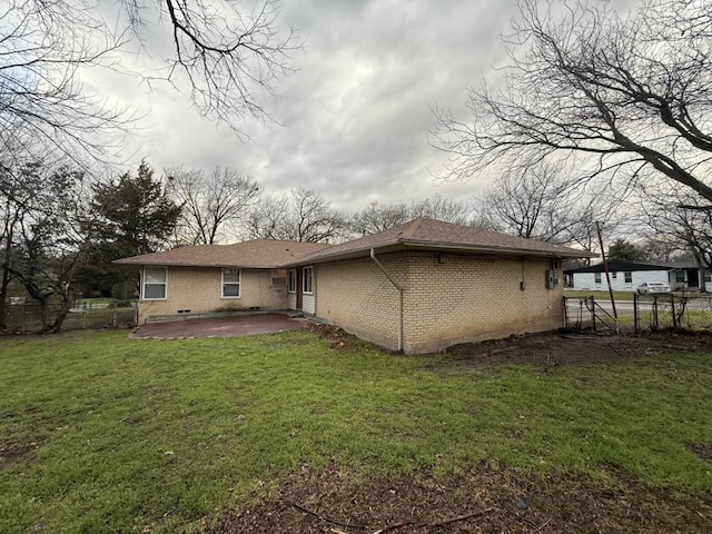 rear view of house featuring brick siding, a lawn, a patio, and fence