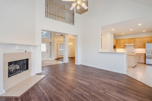 unfurnished living room featuring baseboards, a tiled fireplace, recessed lighting, ceiling fan with notable chandelier, and light wood-style floors