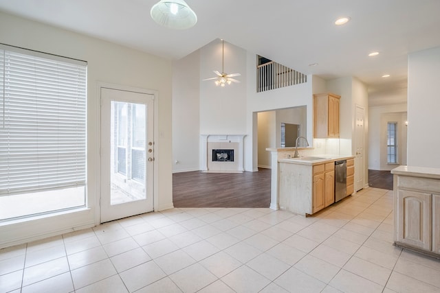 kitchen with light brown cabinets, a high end fireplace, a sink, light countertops, and stainless steel dishwasher