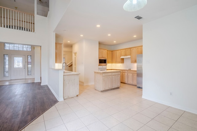 kitchen with visible vents, light brown cabinets, a kitchen island, decorative backsplash, and stainless steel appliances