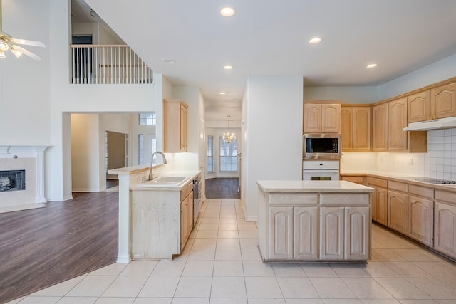 kitchen with under cabinet range hood, a tiled fireplace, light countertops, appliances with stainless steel finishes, and a sink