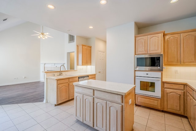 kitchen with light brown cabinets, a kitchen island, light tile patterned floors, stainless steel appliances, and a sink