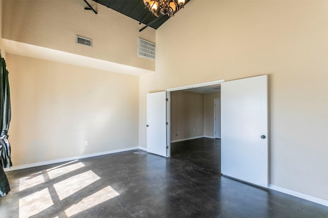 spare room with baseboards, visible vents, finished concrete floors, a towering ceiling, and a chandelier